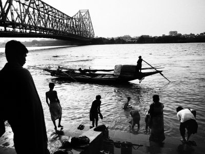 People is ablutioning by Hoogly river down Howrah bridge, where people.
Every day at every hour, day and night, thousends of people cross Howrah bridge. Someone carring good to sell in the city coming from the countryside. Howrah bridge is a crowded and living place. There are hundreds of people standing all the day on Howrah bridge. Someone sells, someone begs, someone slips. 
This is one of the main crossing points of the city.